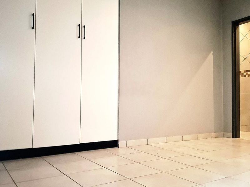 A clean, empty bedroom featuring neutral tiled flooring, built-in cupboards, and simple grey wall finishes.