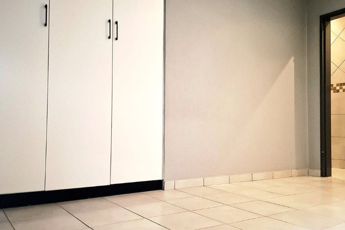 A clean, empty bedroom featuring neutral tiled flooring, built-in cupboards, and simple grey wall finishes.