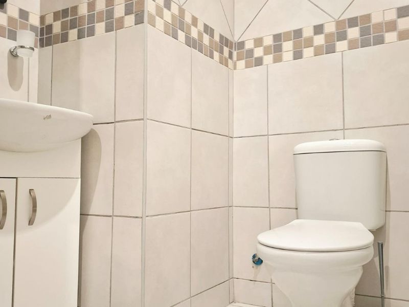 A functional bathroom featuring a white vanity cabinet with a basin, a standard toilet, and neutral ceramic wall and floor tiling.
