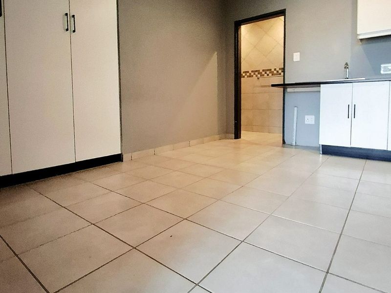 An open-plan living area featuring tiled flooring, built-in cupboards, and a compact kitchen section with cabinetry and a sink.