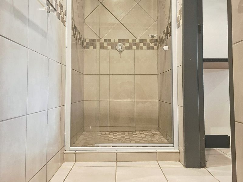 A clean bathroom featuring a glass-enclosed shower with neutral wall and floor tiling and a fitted towel rail.