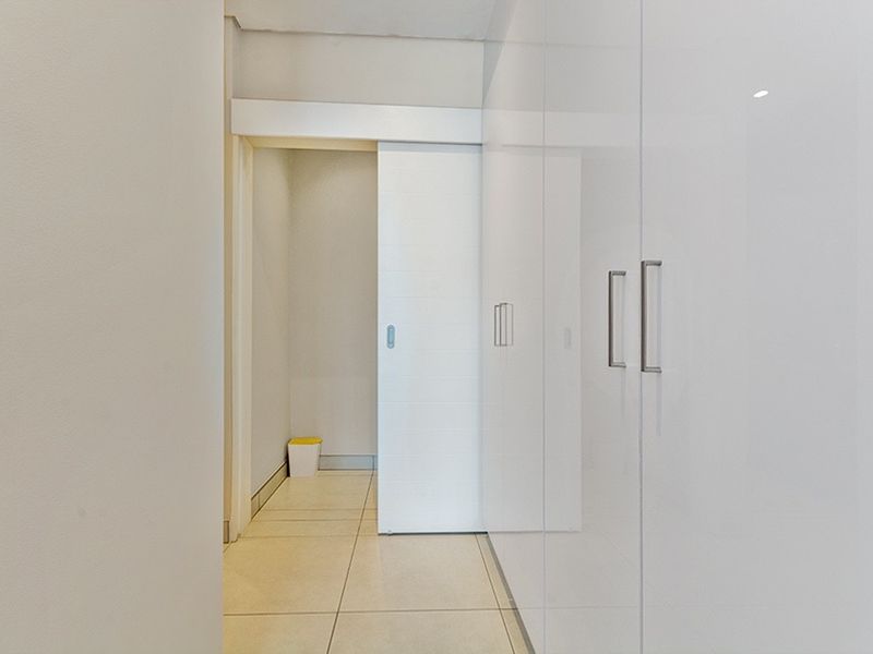 A clean, minimalist hallway featuring high-gloss white built-in cupboards and a modern sliding door, finished with neutral floor tiles.