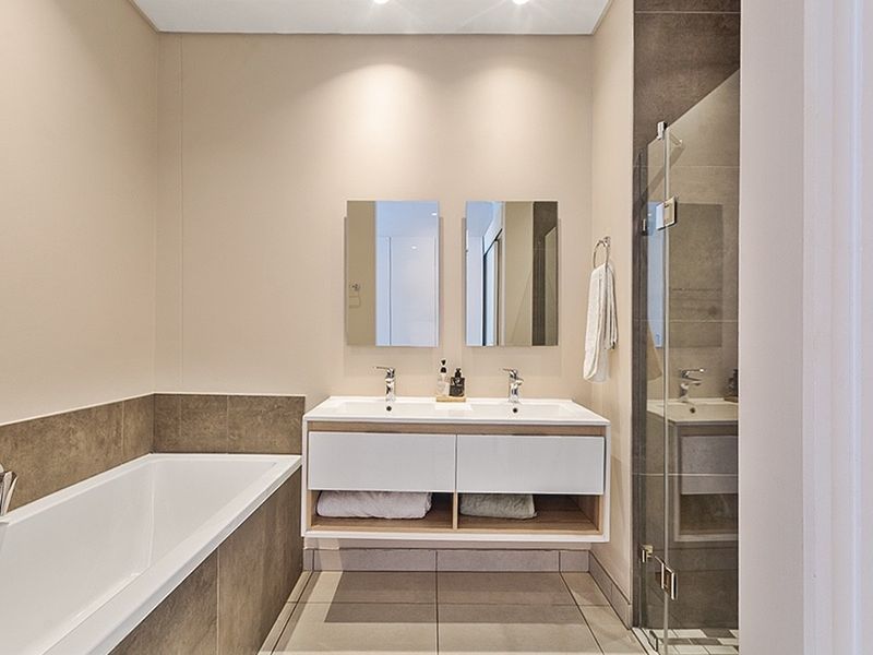 Modern bathroom featuring a double vanity, built-in bathtub, and a separate glass-enclosed shower with contemporary neutral tiling.