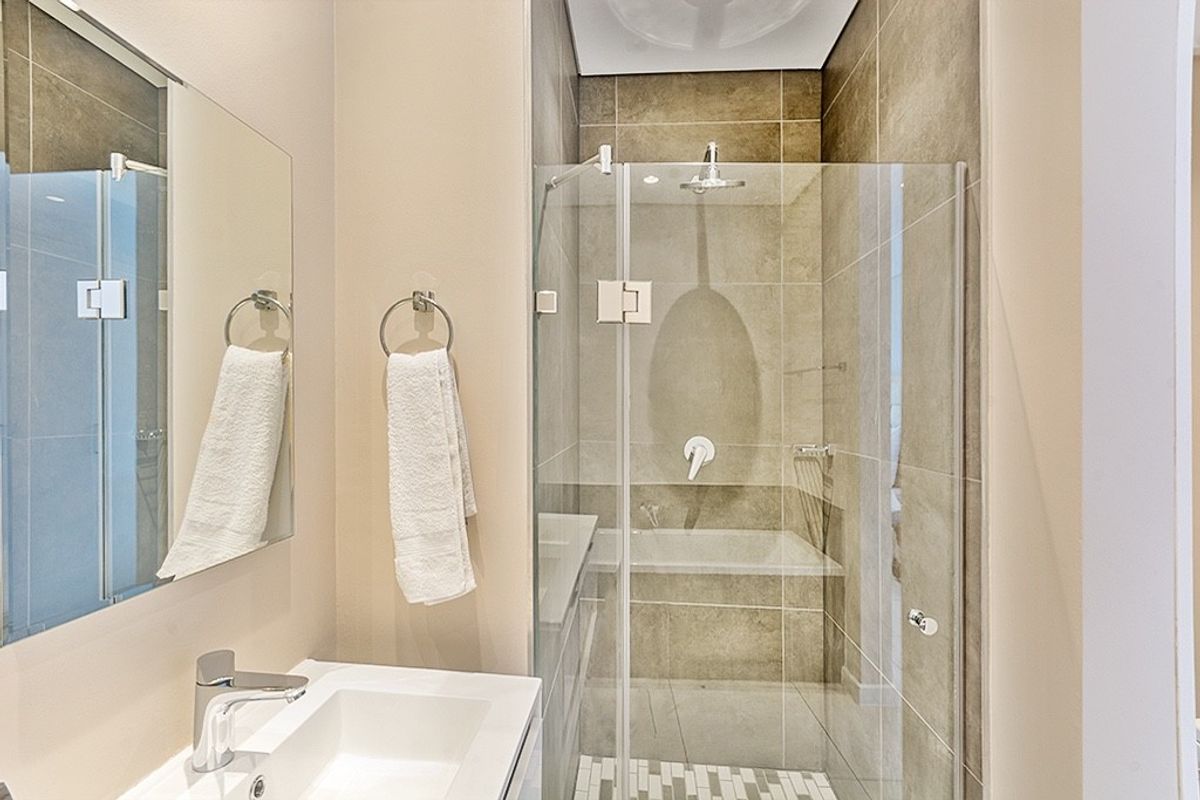 Modern bathroom featuring a glass-enclosed shower with neutral tiling, a wall-mounted basin, and a sleek mirror.