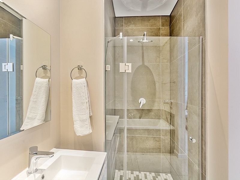 Modern bathroom featuring a glass-enclosed shower with neutral tiling, a wall-mounted basin, and a sleek mirror.