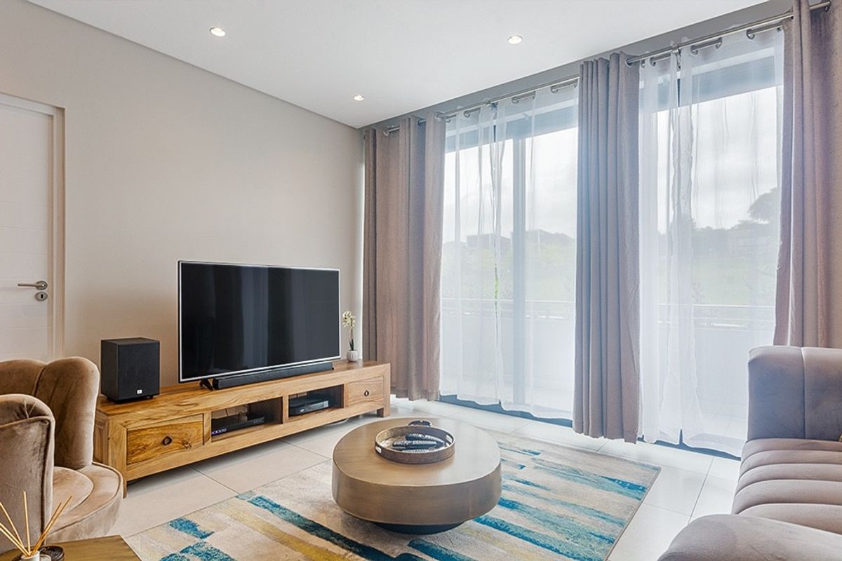 A bright and modern living room featuring tiled flooring, recessed lighting, and large sliding glass doors that provide access to the balcony.