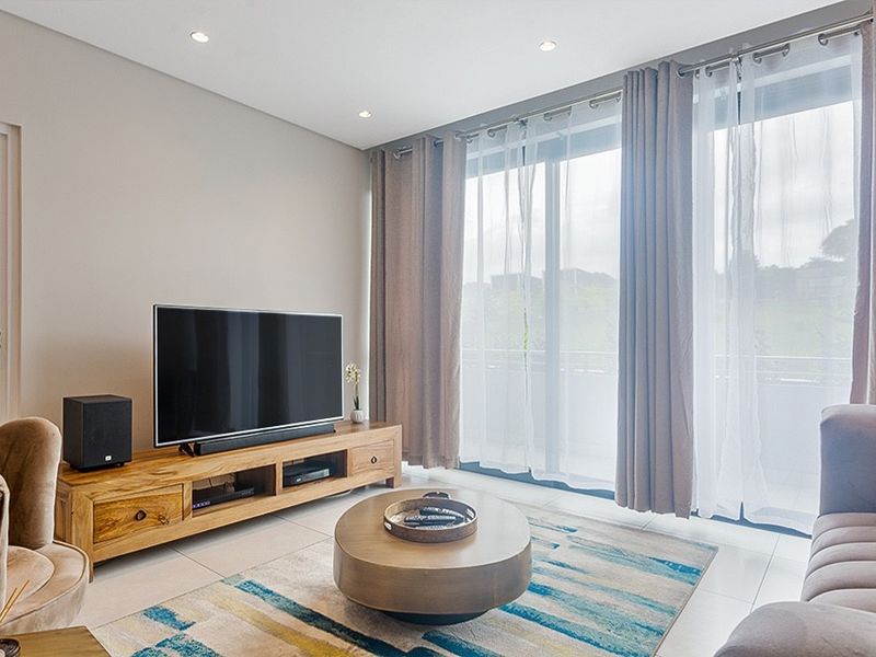 A bright and modern living room featuring tiled flooring, recessed lighting, and large sliding glass doors that provide access to the balcony.