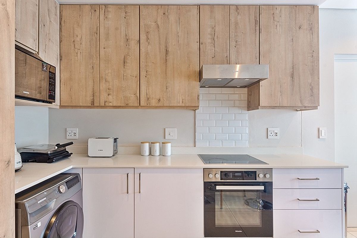 Modern kitchen featuring light wood-grain upper cabinetry, white lower cabinets, stone countertops, subway tile backsplash, and integrated appliances including an oven and hob.