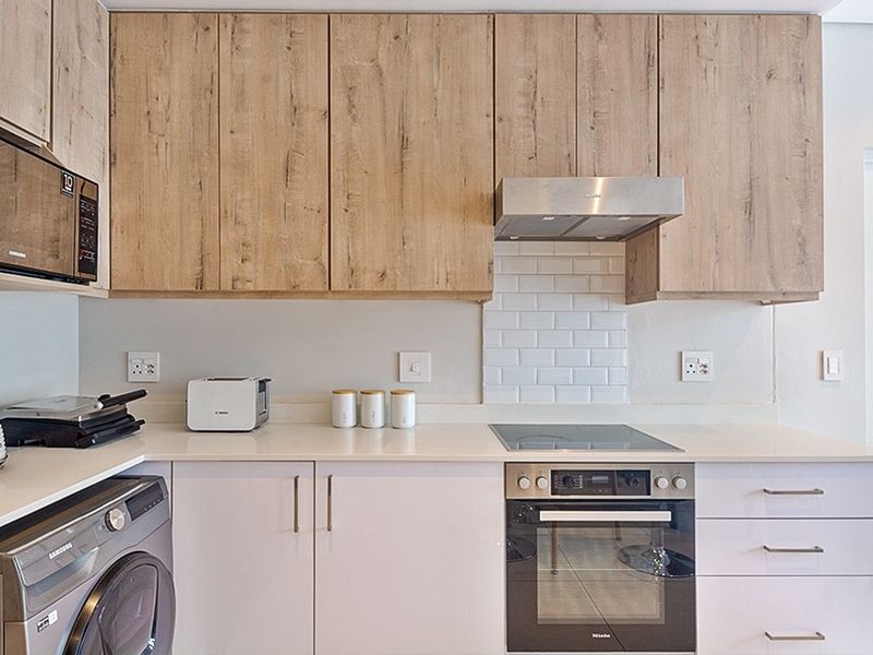 Modern kitchen featuring light wood-grain upper cabinetry, white lower cabinets, stone countertops, subway tile backsplash, and integrated appliances including an oven and hob.