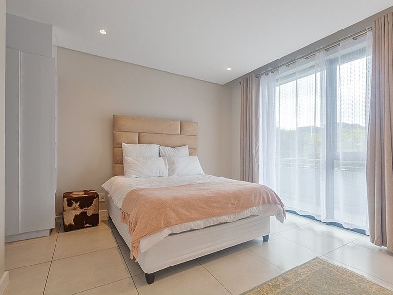 A bright and modern bedroom featuring tiled flooring, built-in cupboards, and a large sliding glass door providing access to an outdoor area.