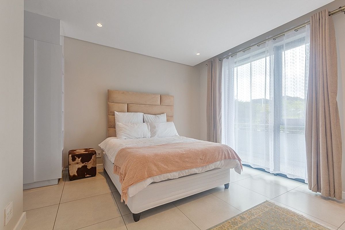 A bright and modern bedroom featuring tiled flooring, built-in cupboards, and a large sliding glass door providing access to an outdoor area.
