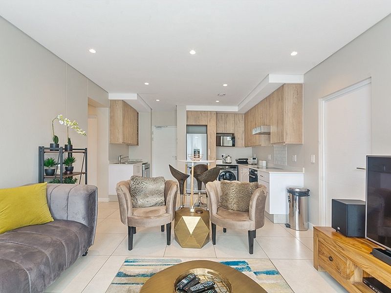 Modern open-plan living area featuring a contemporary kitchen with built-in cabinetry, integrated appliances, and sleek tiled flooring throughout.
