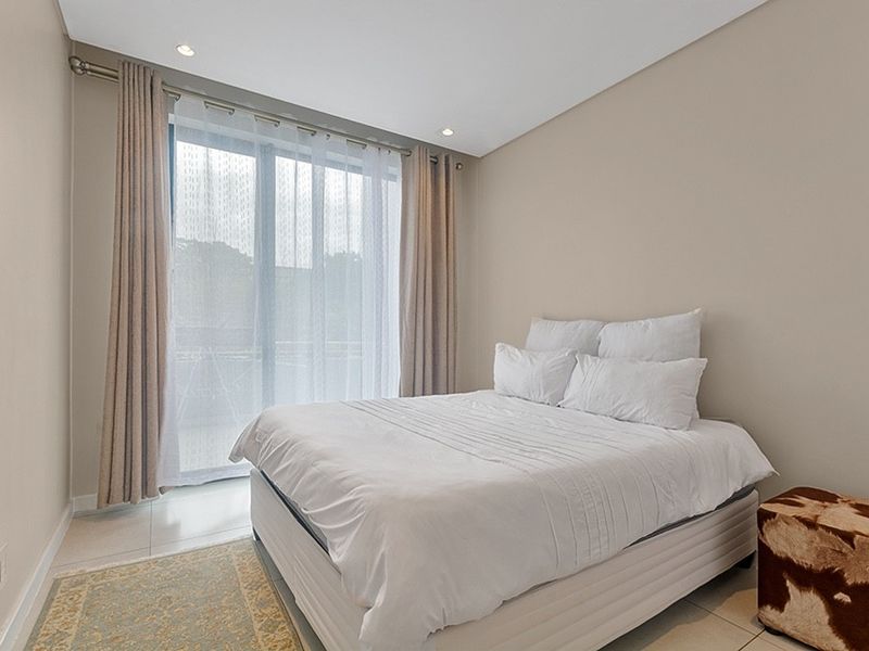 A bright and modern bedroom featuring neutral walls, tiled flooring, recessed lighting, and a large sliding glass door providing natural light.