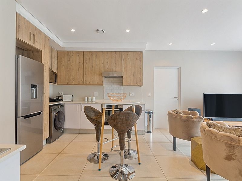 Modern open-plan living area featuring a contemporary kitchen with wood-finish cabinetry, subway tile backsplash, and integrated appliances, flowing into a bright living space.