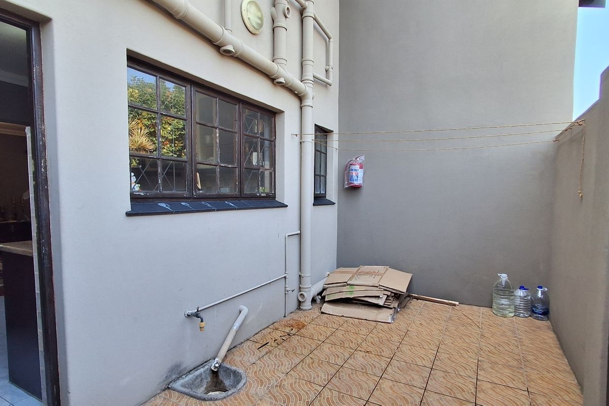 A paved rear courtyard area featuring external plumbing, a wall-mounted fire extinguisher, and direct access to the interior living space.