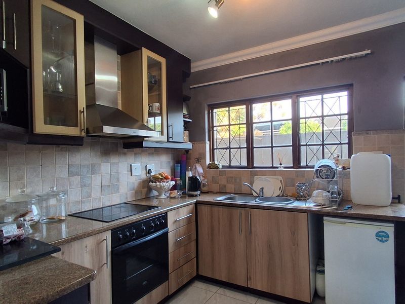 Functional kitchen featuring wood-look cabinetry, stone-effect countertops, tiled backsplash, and integrated cooking appliances with a window overlooking the exterior.