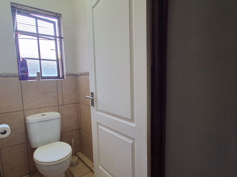 A functional bathroom featuring tiled walls and flooring, a standard toilet, and a window with fitted blinds.