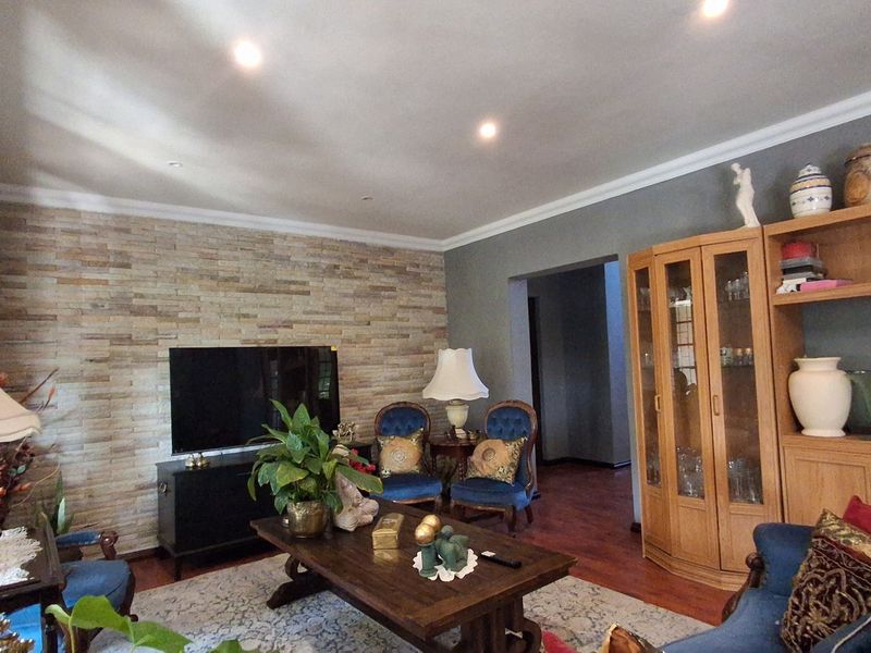 A comfortable living room featuring a textured stone accent wall, recessed downlighting, crown molding, and warm hardwood flooring.