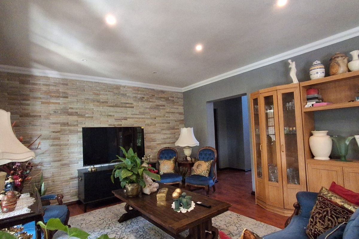 A comfortable living room featuring a textured stone accent wall, recessed downlighting, crown molding, and warm hardwood flooring.