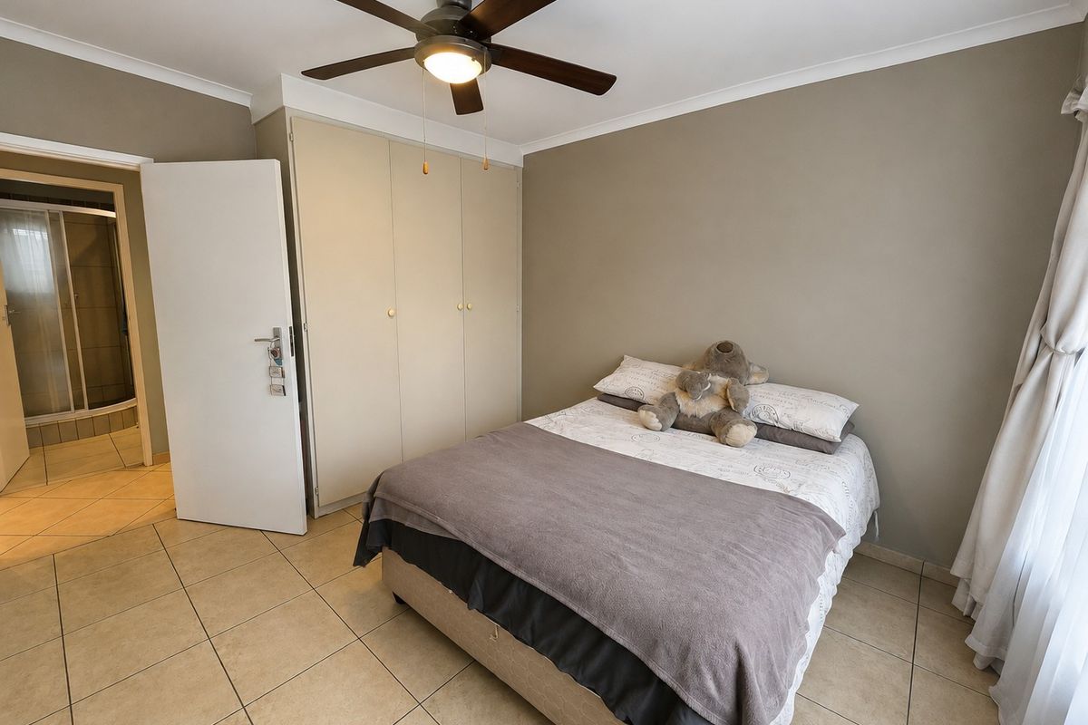 A bedroom featuring tiled flooring, built-in cupboards, and a ceiling fan, with direct access to an en-suite bathroom.