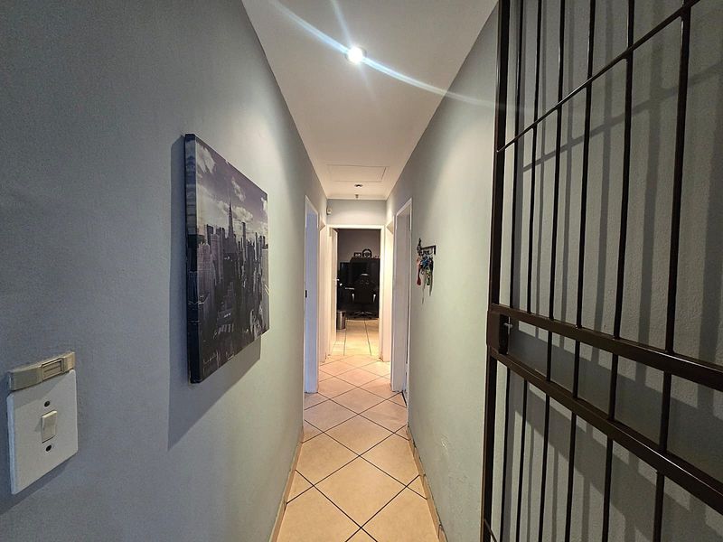 A functional hallway featuring tiled flooring, a security gate, and a ceiling access hatch, providing access to the interior rooms of the home.