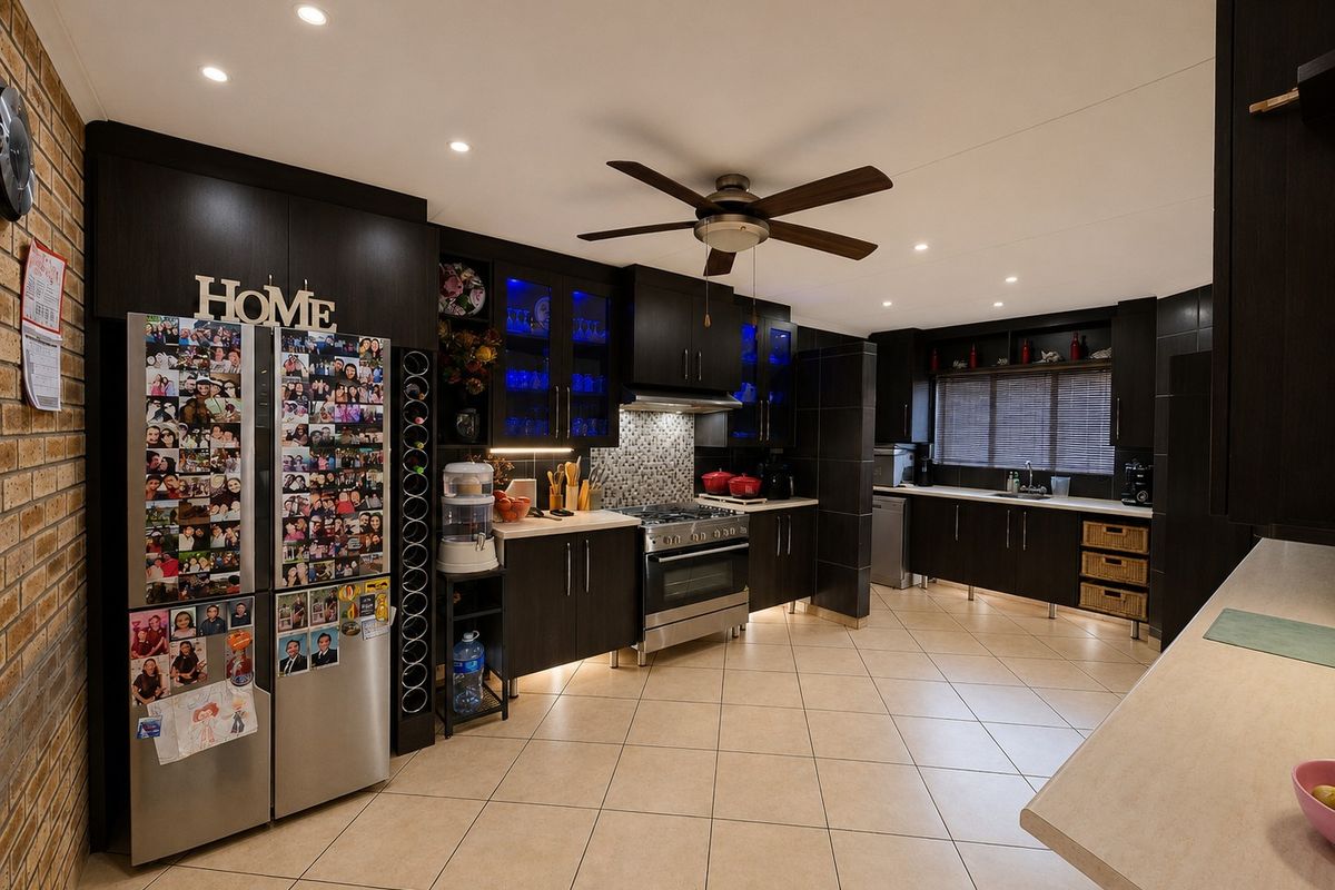Spacious modern kitchen featuring dark wood cabinetry, gas stove, tiled flooring, and an exposed brick feature wall with ample storage and workspace.