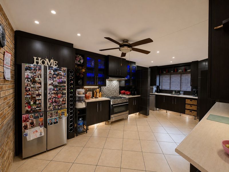 Spacious modern kitchen featuring dark wood cabinetry, gas stove, tiled flooring, and an exposed brick feature wall with ample storage and workspace.