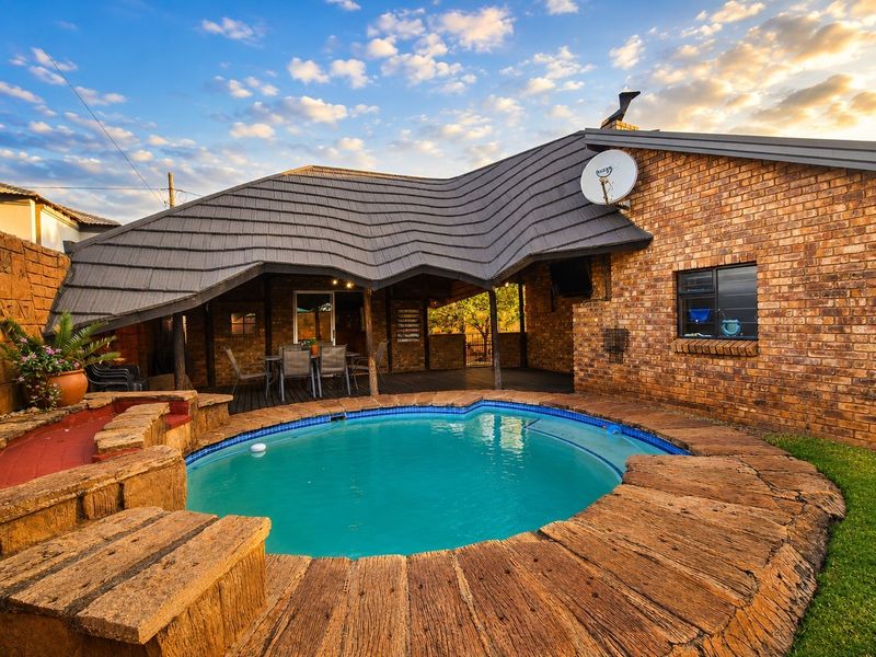 Outdoor entertainment area featuring a swimming pool with stone-look coping, adjacent to a covered patio with brick wall finishes and a tiled roof.