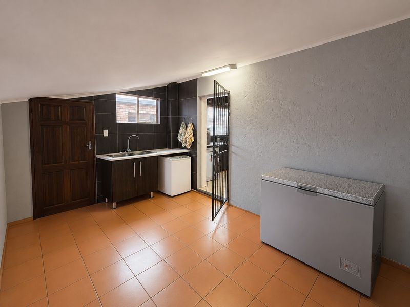 A functional laundry room featuring tiled flooring, a built-in sink with dark cabinetry, and a security gate leading to an exterior area.