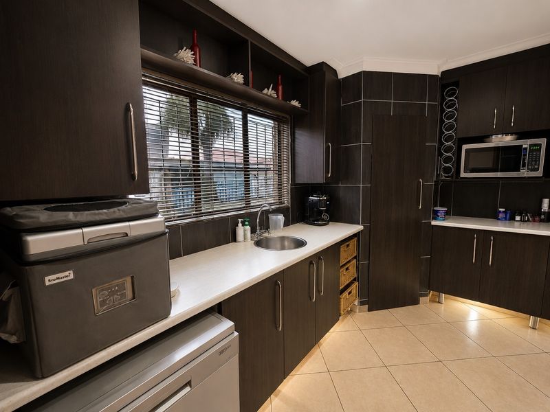 A functional scullery featuring dark wood cabinetry, laminate countertops, a stainless steel sink, and built-in microwave with integrated under-cabinet lighting.