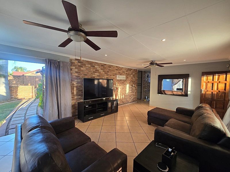 Spacious living room featuring an exposed brick accent wall, tiled flooring, ceiling fans, and direct access to the outdoor patio area.