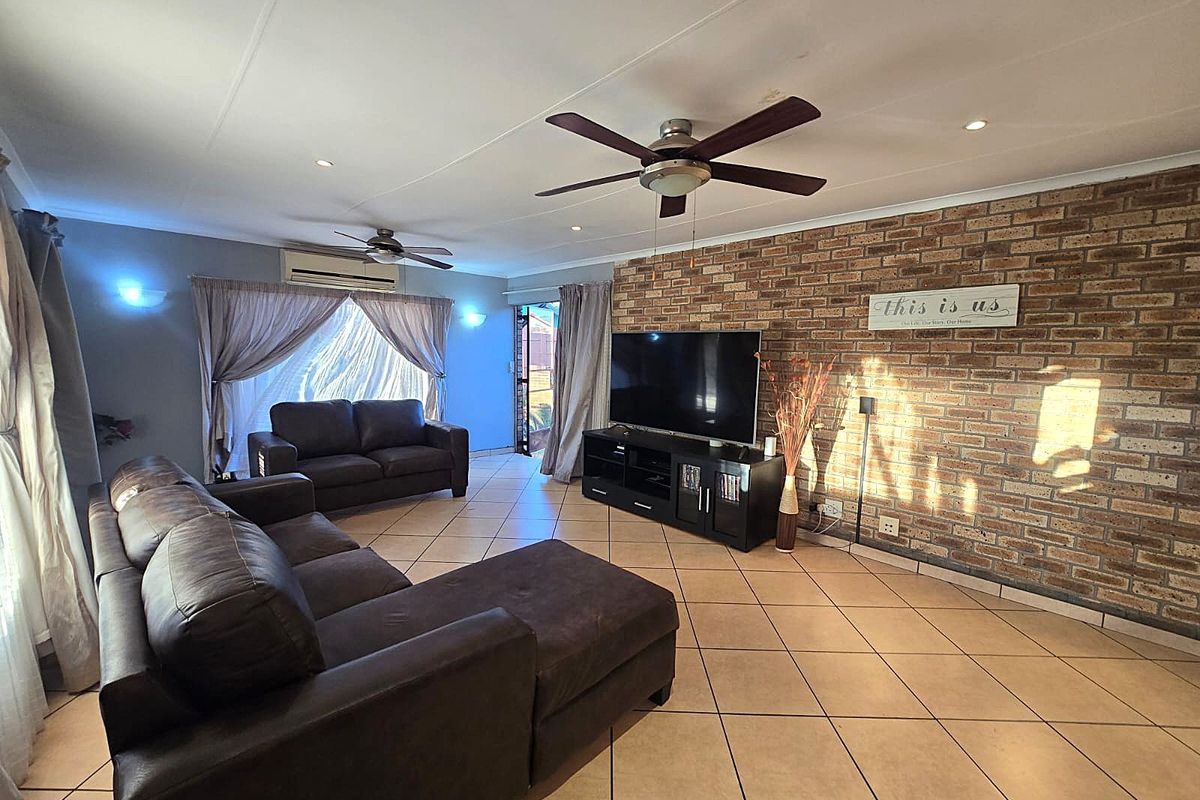 Spacious living room featuring an exposed brick accent wall, tiled flooring, ceiling fans, and a wall-mounted air conditioning unit.