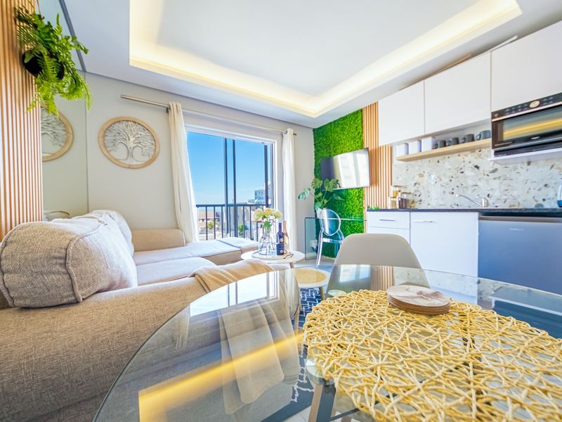 Modern open-plan living area featuring a compact kitchen with terrazzo backsplash, integrated microwave, and direct access to a balcony with natural light.
