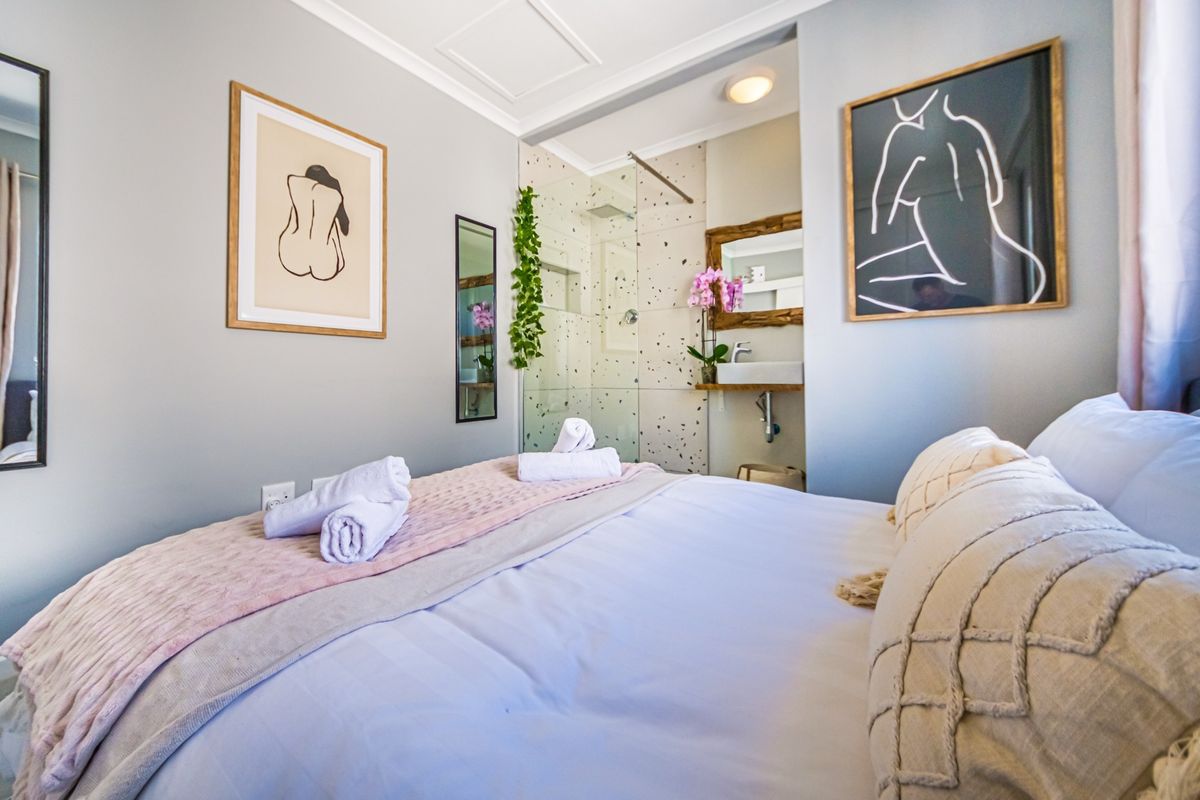 A modern bedroom featuring an open-plan en-suite bathroom with a glass-enclosed shower and wall-mounted basin, finished with contemporary fixtures.