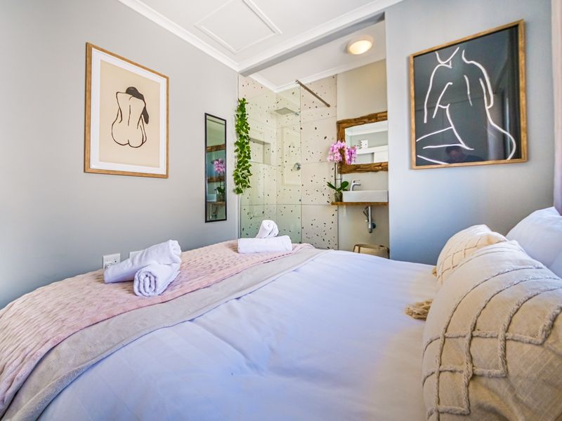 A modern bedroom featuring an open-plan en-suite bathroom with a glass-enclosed shower and wall-mounted basin, finished with contemporary fixtures.