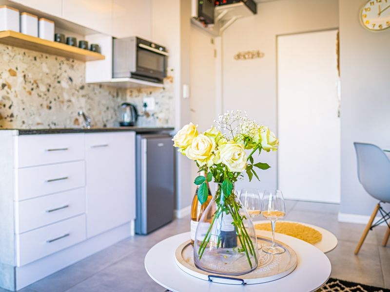 A modern open-plan kitchen area featuring white cabinetry, a stylish terrazzo backsplash, and sleek tiled flooring, creating a bright and functional living space.
