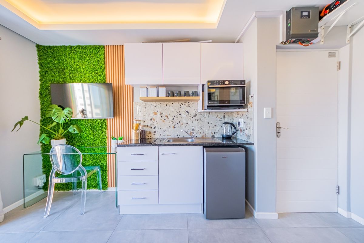 Compact modern kitchen featuring white cabinetry, a stylish terrazzo backsplash, built-in microwave, and integrated sink, complemented by decorative slatted wood and green wall paneling.