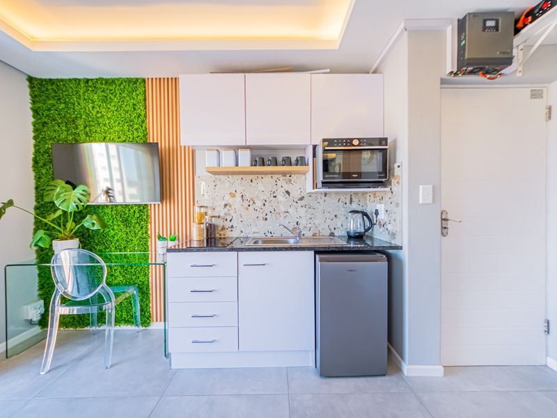 Compact modern kitchen featuring white cabinetry, a stylish terrazzo backsplash, built-in microwave, and integrated sink, complemented by decorative slatted wood and green wall paneling.