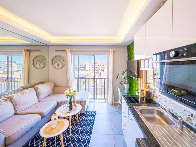Modern open-plan living area featuring a compact, well-equipped kitchen with integrated appliances, sleek cabinetry, and direct access to a private balcony.
