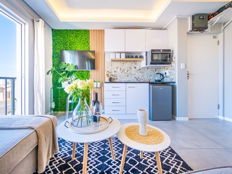 Modern open-plan living area featuring a compact kitchenette with built-in cabinetry, terrazzo backsplash, and stylish feature walls with integrated lighting.