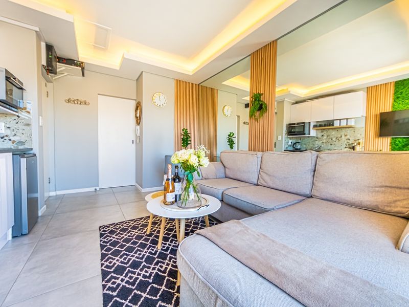 Modern open-plan living area featuring contemporary kitchen cabinetry, stylish timber slat accents, mirrored walls, and recessed ceiling lighting with neutral tiled flooring.