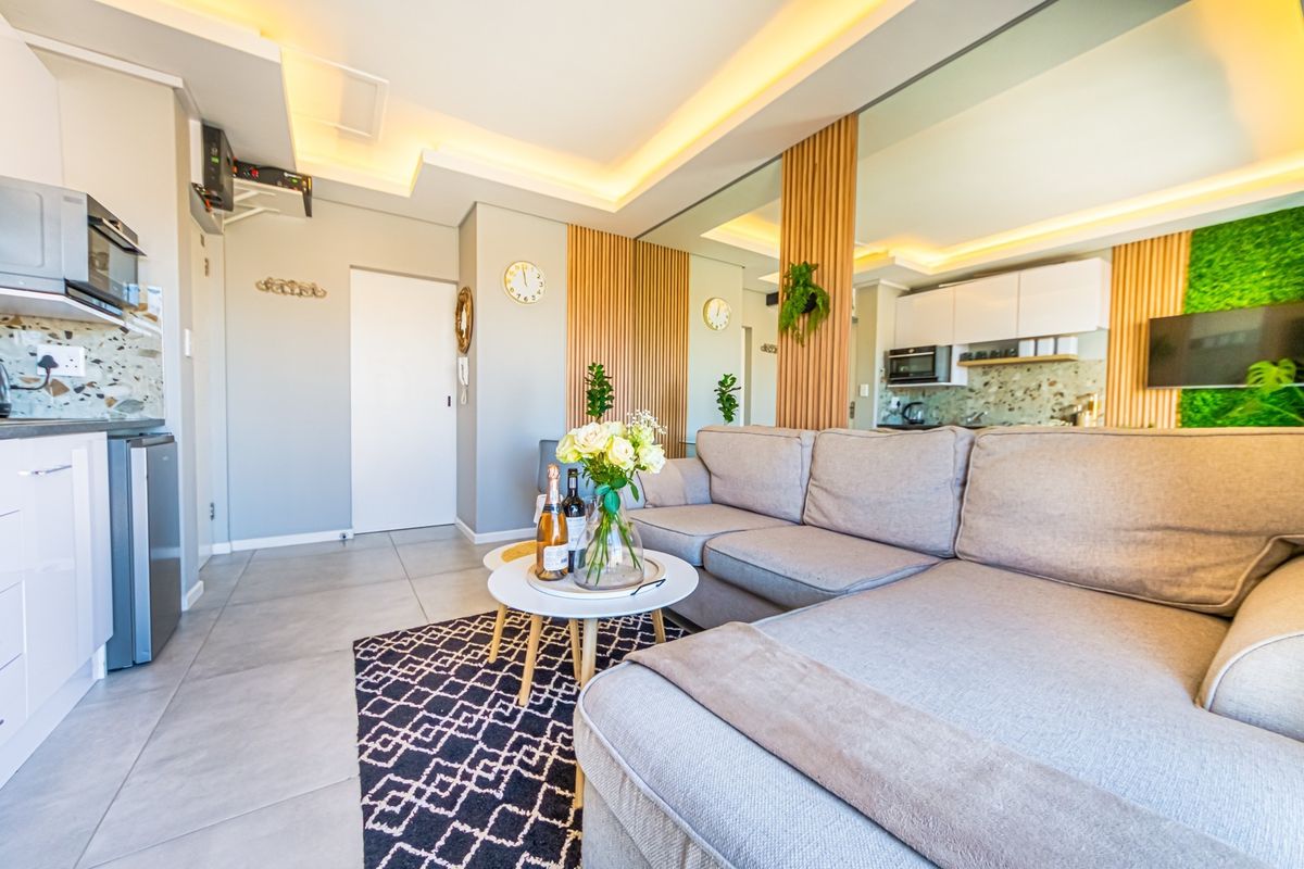 Modern open-plan living area featuring contemporary kitchen cabinetry, stylish timber slat accents, mirrored walls, and recessed ceiling lighting with neutral tiled flooring.