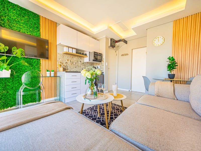 A modern open-plan living and kitchen area featuring contemporary cabinetry, a stylish terrazzo backsplash, recessed lighting, and decorative wood and green wall accents.