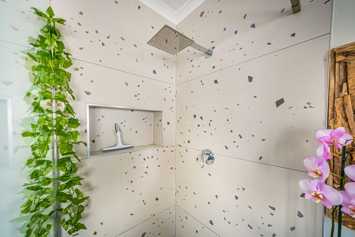 Modern shower enclosure featuring contemporary terrazzo-style wall tiles, a built-in recessed niche, and a sleek square rainfall shower head.