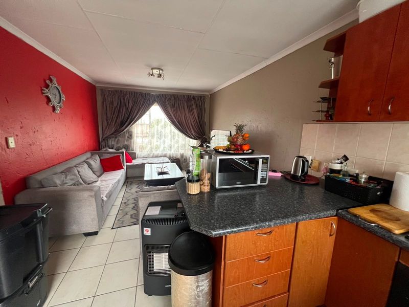 Open-plan living area featuring a compact kitchen with laminate cabinetry and tiled flooring, seamlessly connected to the adjacent living space.