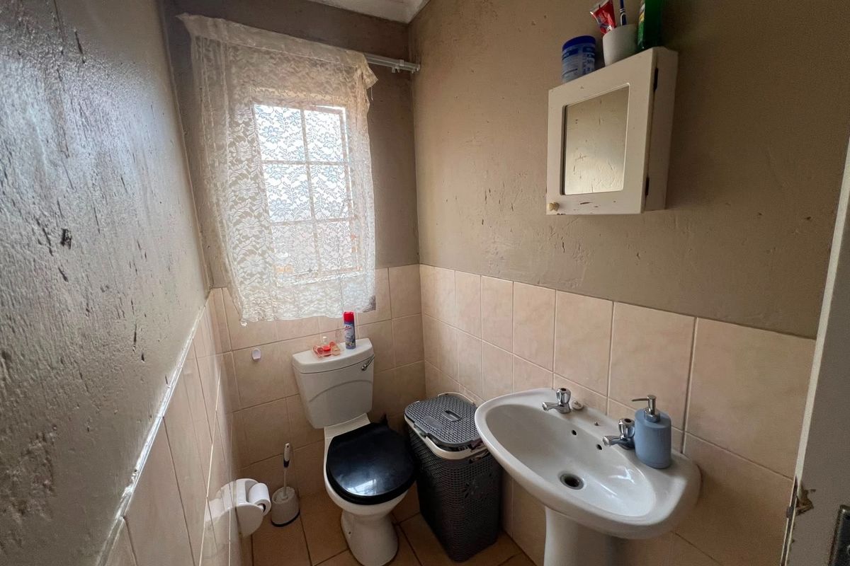 A compact bathroom featuring a pedestal basin, toilet, and tiled finishes, requiring cosmetic updates to improve the overall aesthetic and condition.