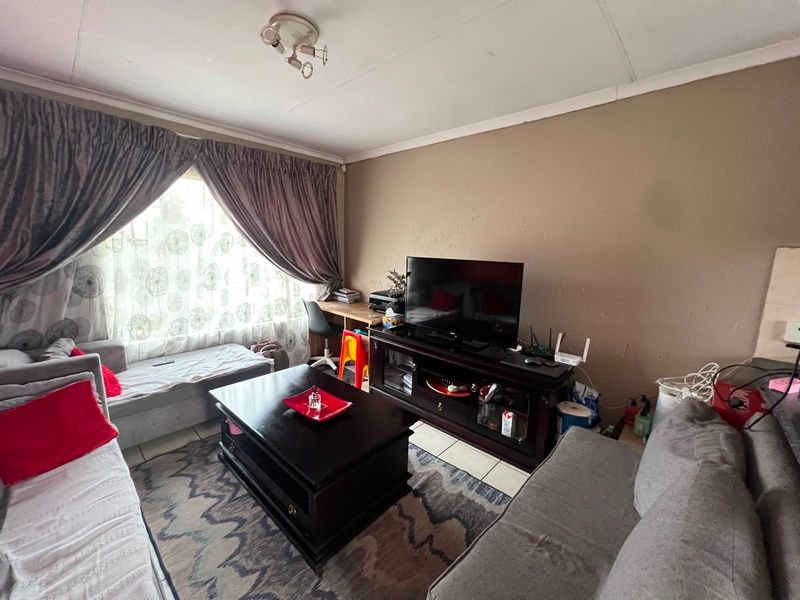 A living room featuring tiled flooring and a ceiling light fixture, with visible wear on the wall surfaces.