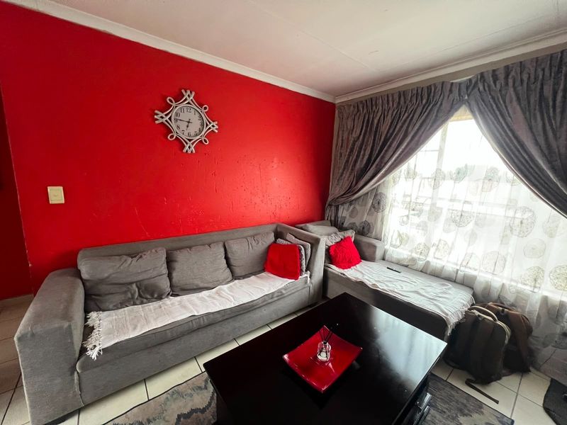 A living room featuring tiled flooring and a large window with curtain tracks, currently finished with a bold red accent wall.