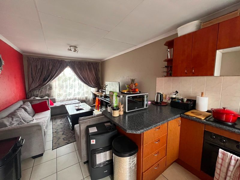 Open-plan living area featuring a compact kitchen with built-in cabinetry and tiled flooring, seamlessly flowing into the adjacent lounge space.