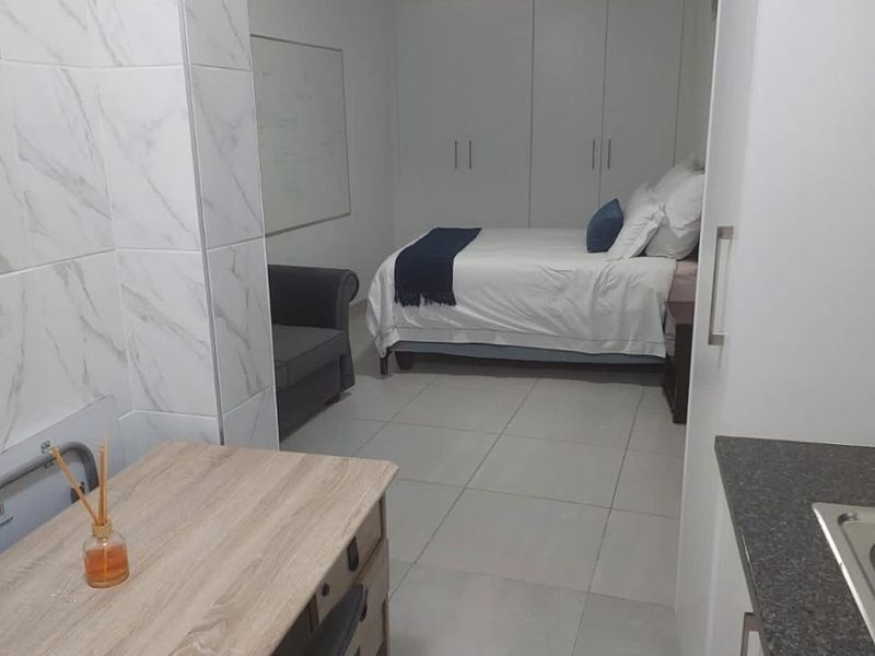 Open-plan studio layout featuring tiled flooring, built-in bedroom cupboards, and a compact kitchen area with stone-look countertops.